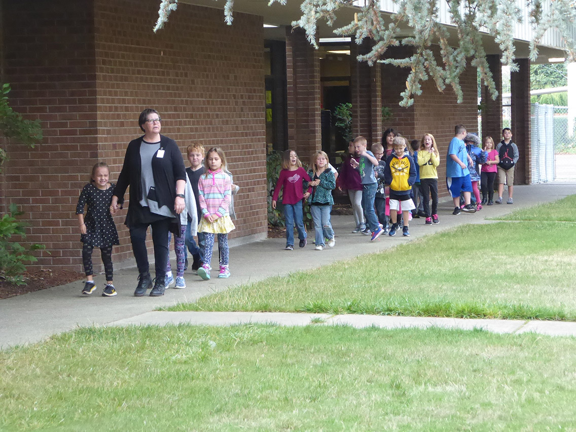 Students walking in a line on a sidewalk next to the school